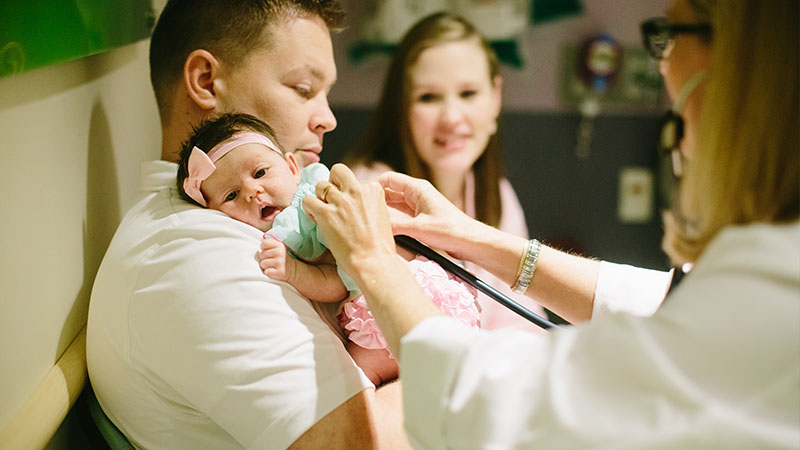 doctor listens to baby's heart with parents