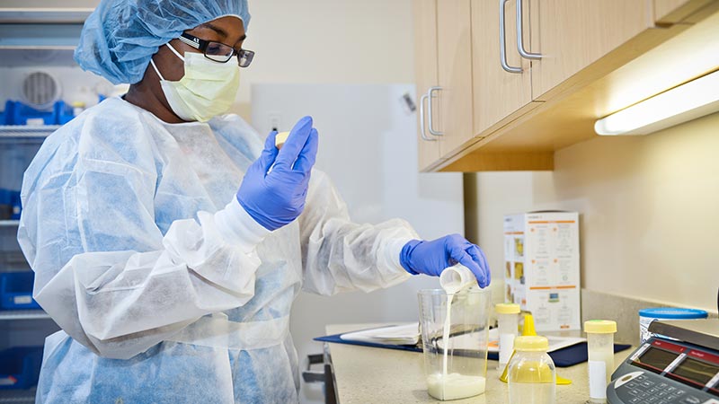 A Human Milk Lab Tech pours EBM (expressed breast milk) into another container to get the correct amount and mix in any additives needed to supplement the milk's nutritional value.